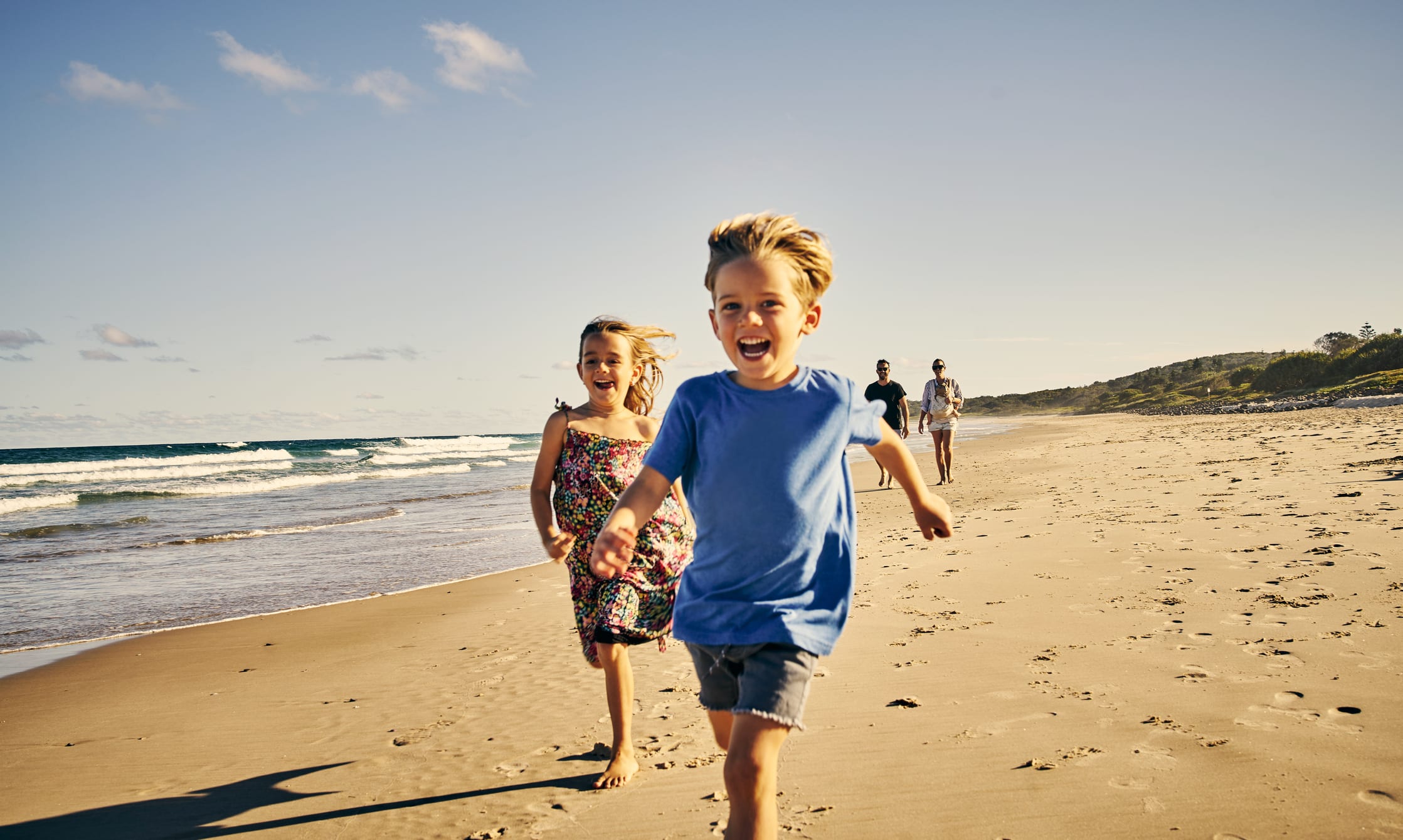 Shot of two little children running at the beach with their parents