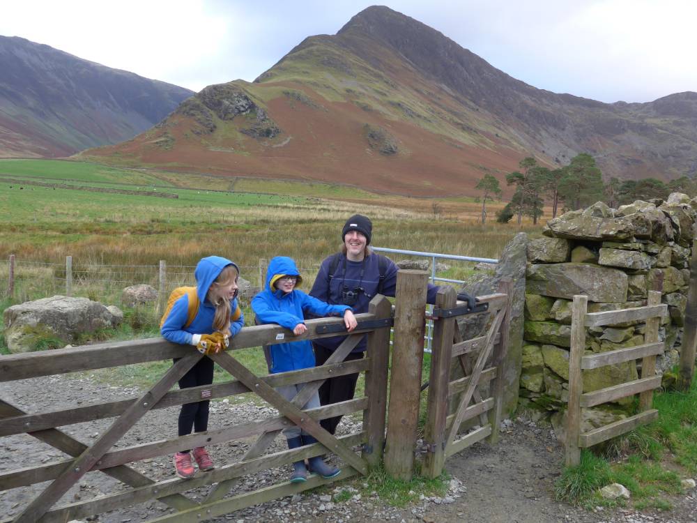 Family stands behind a gate, with the Keswick mountains in the background