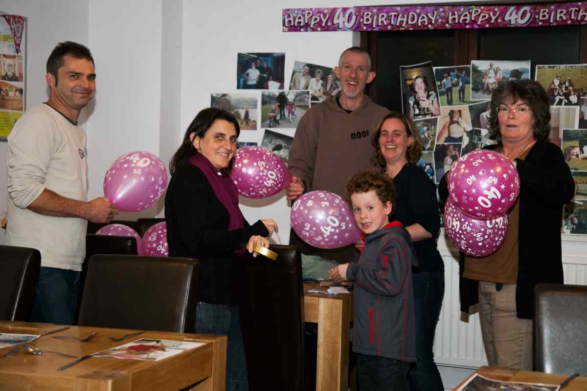 A group of people holding birthday balloons smiling at the camera