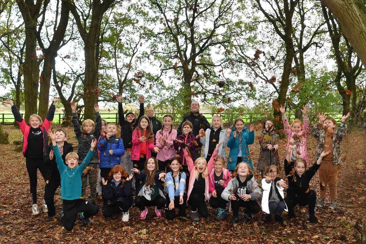 Children throwing leaves and smiling on a school trip