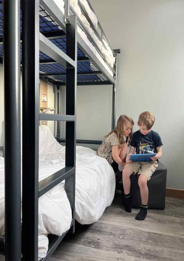 Two children sat on a bunk bed playing on their iPad