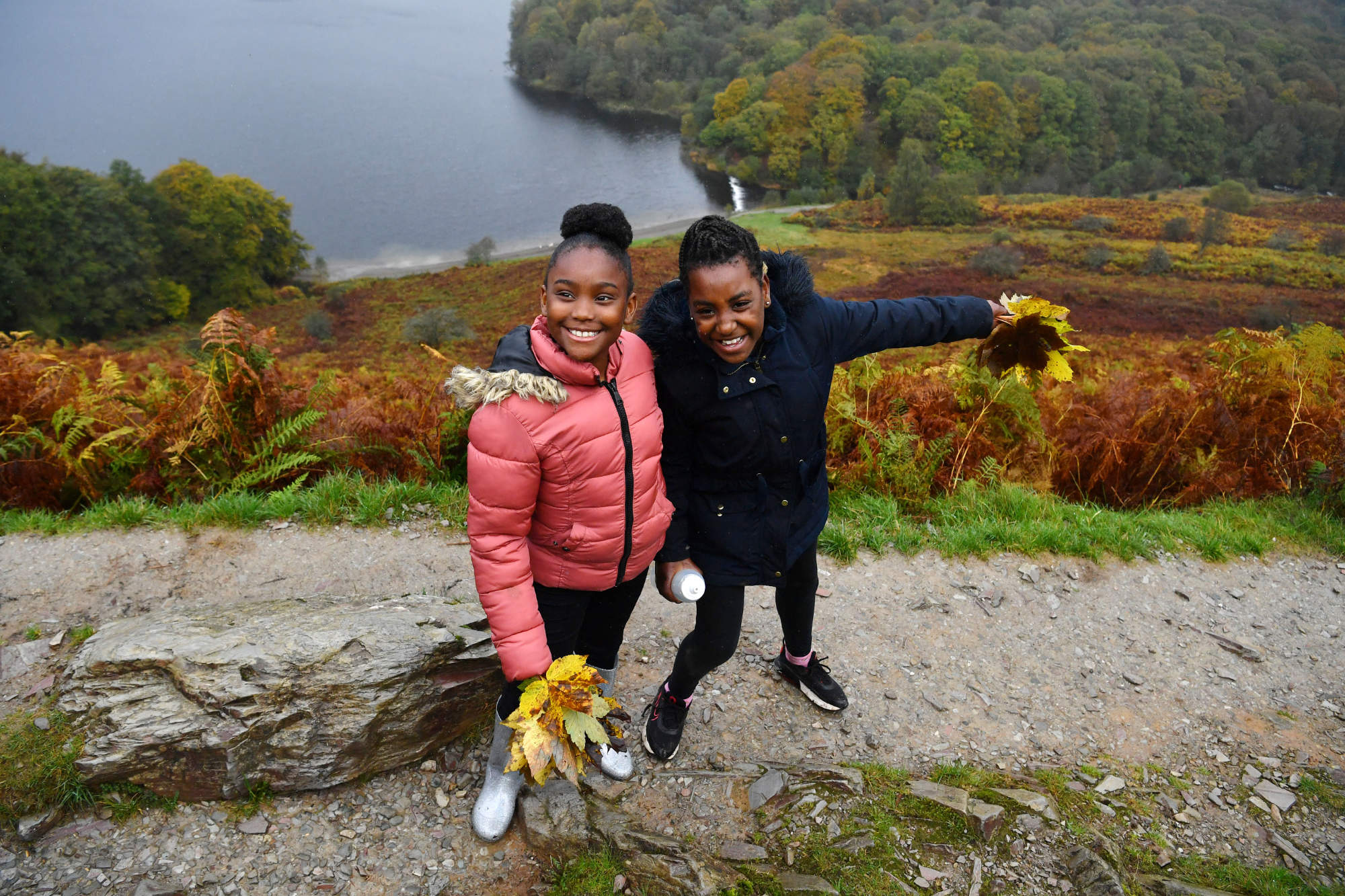 Two children stood on a trail holding bunches of leaves and smiling